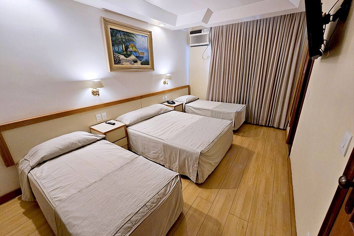 Ein Hotelzimmer mit drei Betten, einem Bild an der Wand, einer Klimaanlage und einem Vorhang.