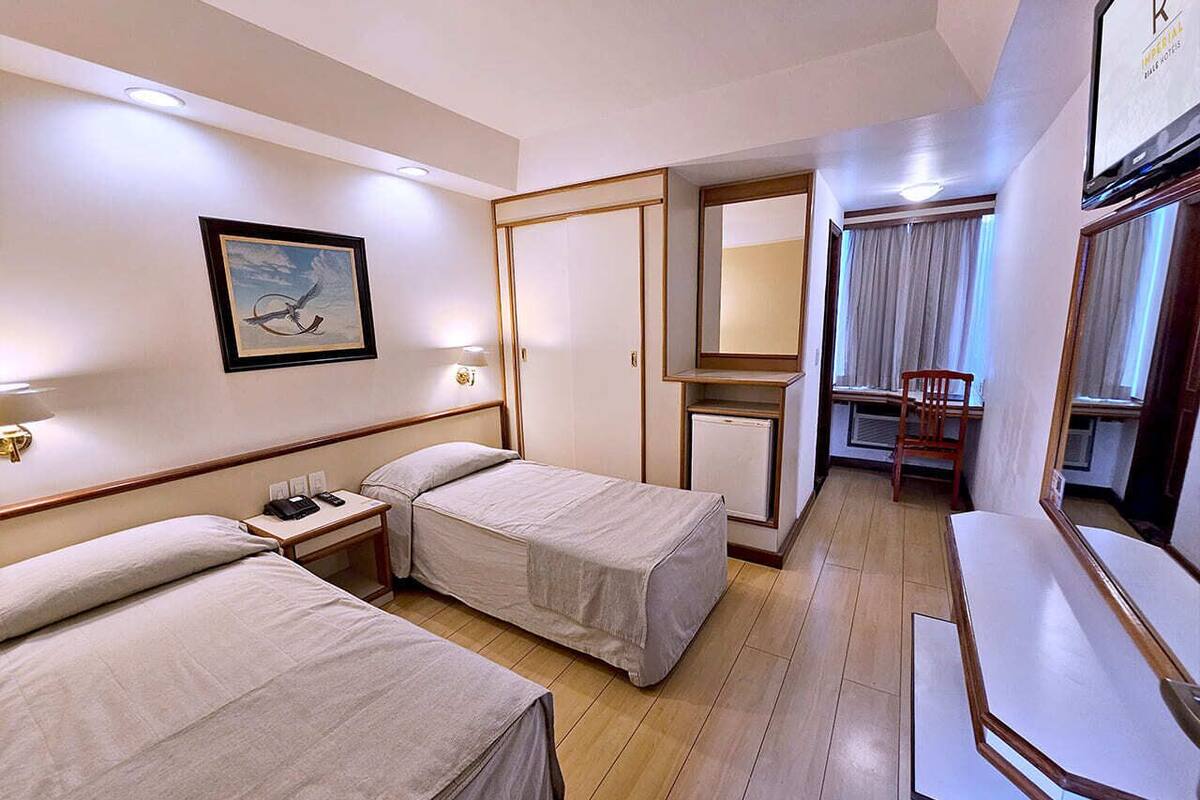 Ein Hotelzimmer mit zwei Betten, einem Schreibtisch, einem Stuhl, einem Spiegel und einem Bild an der Wand.