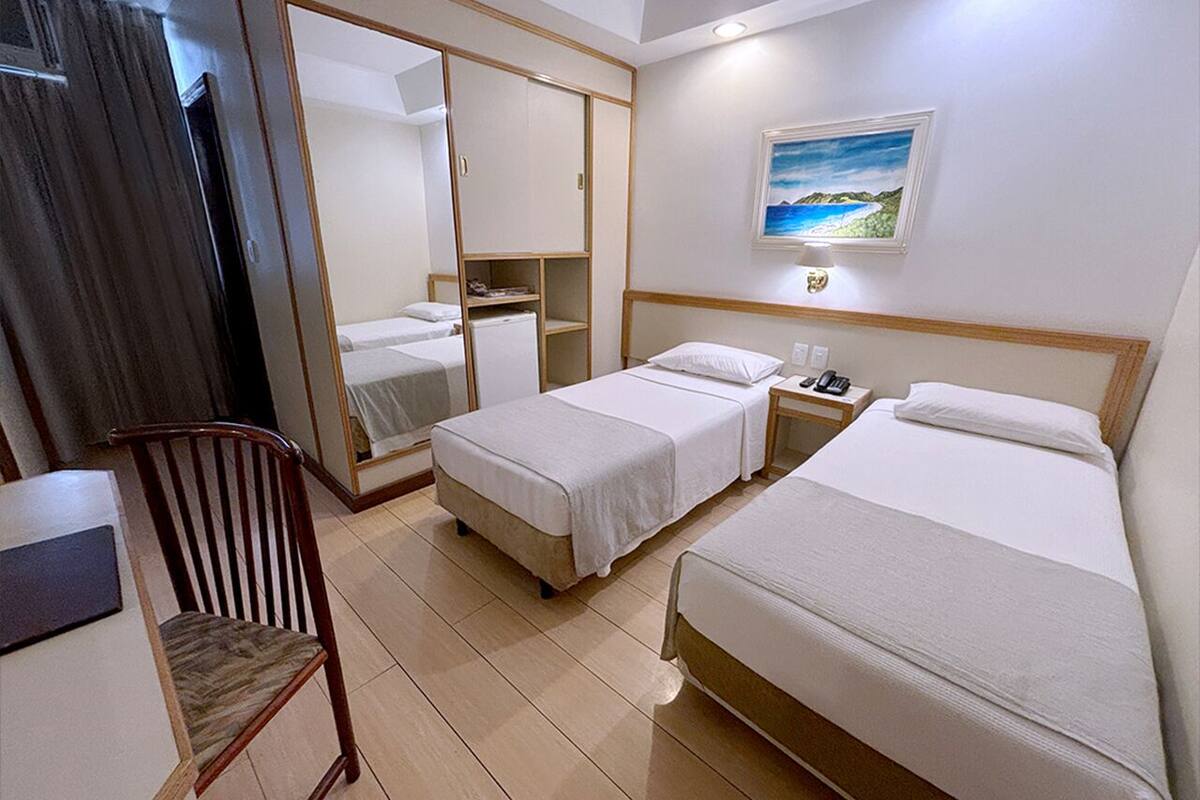 Ein Hotelzimmer mit zwei Einzelbetten, einem Schreibtisch mit Stuhl, einem Kleiderschrank und einem Bild an der Wand.