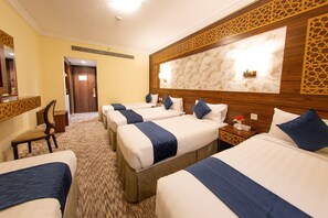 Une chambre d’hôtel avec quatre lits, une tête de lit en bois, un mur en marbre et un sol recouvert de moquette.