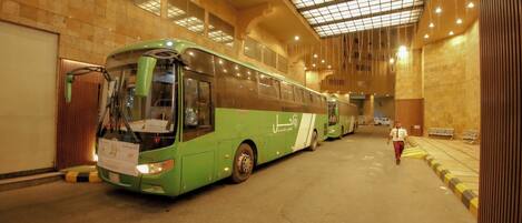 En grön buss står parkerad inuti en byggnad med ett klinkergolv och ett högt tak med ett rutmönster.