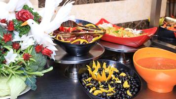 A table with various dishes, including a bowl of black beans with yellow pieces, a bowl of sliced vegetables, and a red dish with mixed ingredients.