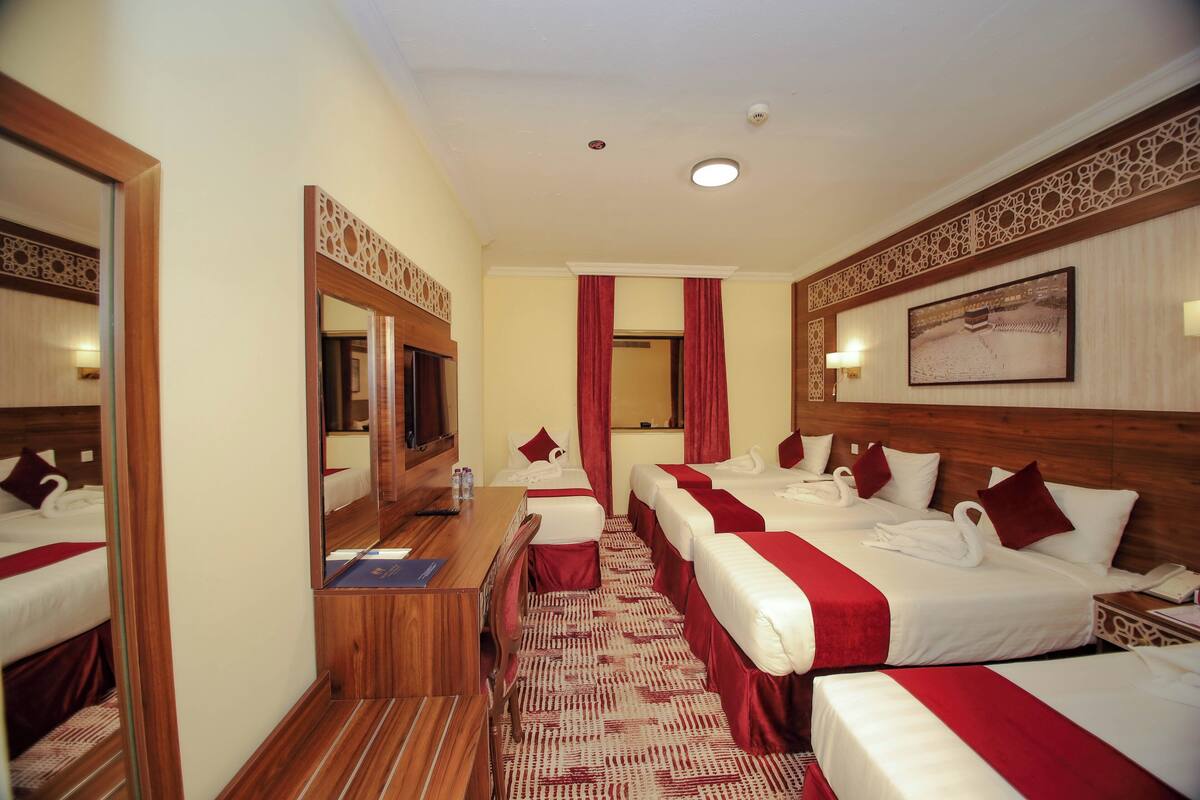 A hotel room with a wooden desk, two beds with red and white bedding, a mirror, and a patterned carpet.