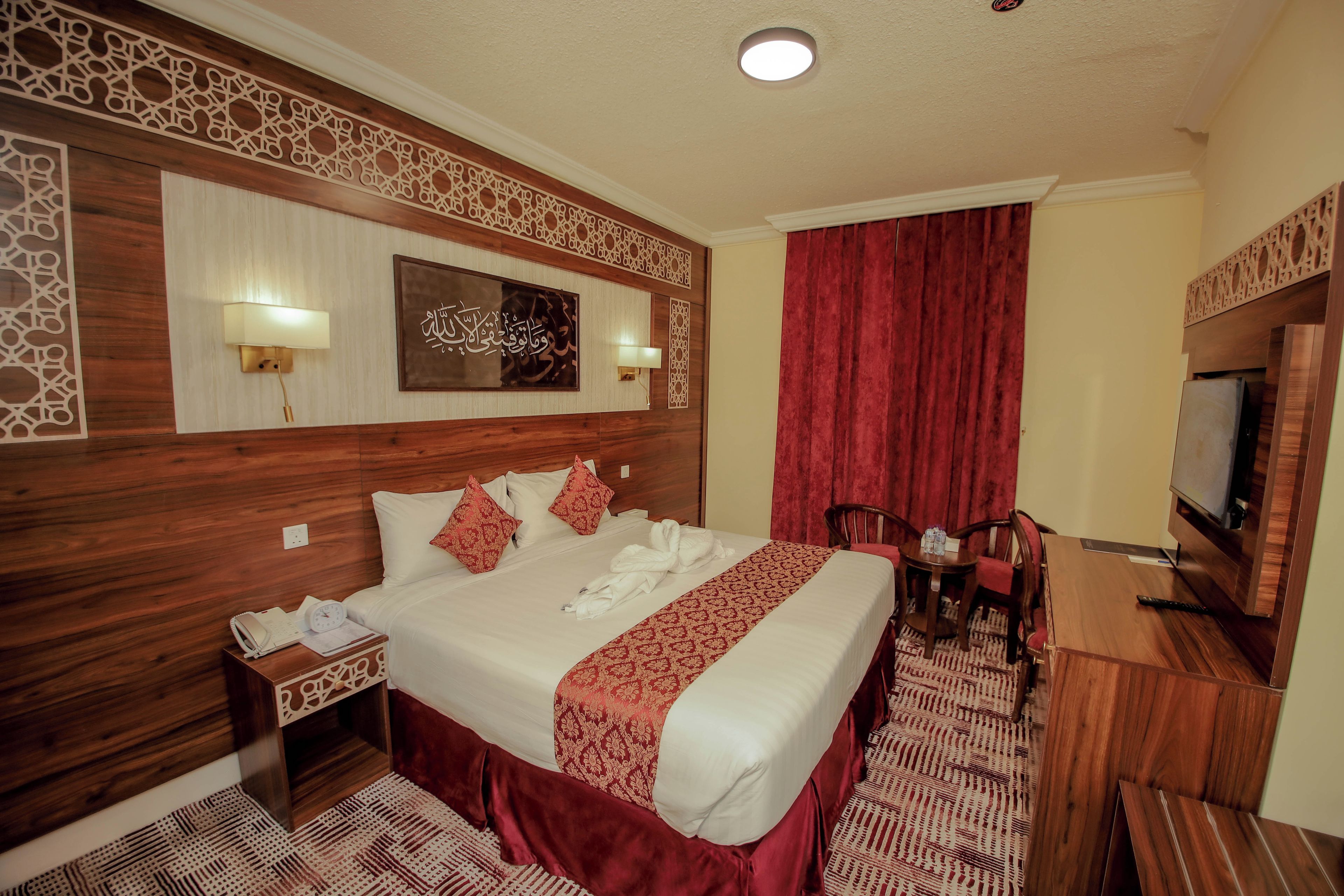 A hotel room with a large bed, a desk with a chair, a television, and decorative wall panels.