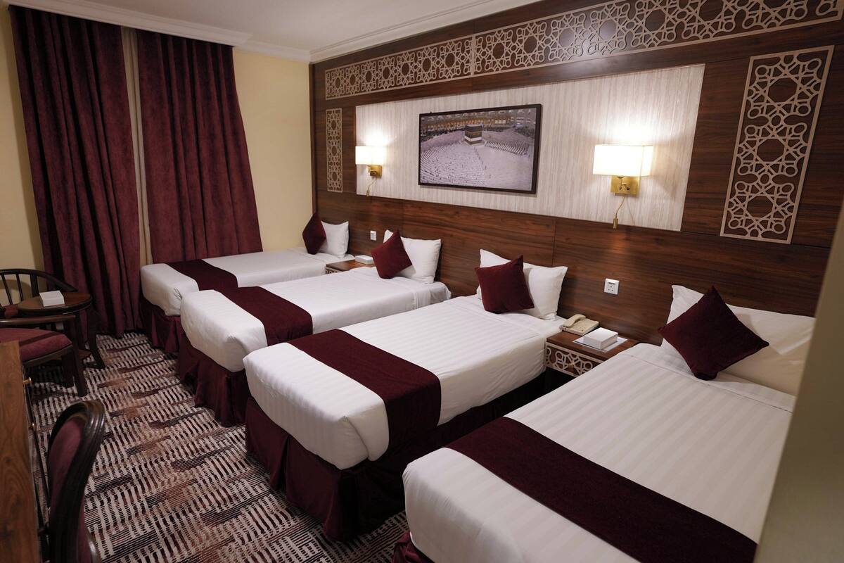 A hotel room with four single beds, a desk, and a chair.