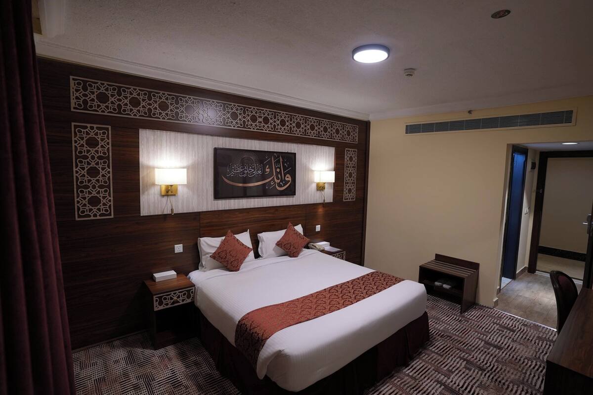 A hotel room with a large bed, two bedside lamps, a decorative headboard, and a wall-mounted artwork.