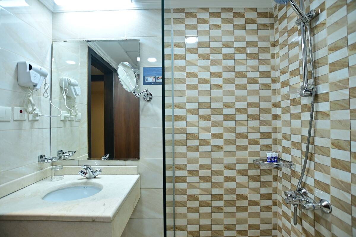 A bathroom with a sink, mirror, hairdryer, and shower.