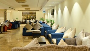 A spacious lobby with rows of blue sofas and armchairs, each with beige and gray cushions. There are potted plants and a flat-screen TV mounted on the wall. - Abraj Al Tayseer Tuwa Hotel (Makkah)