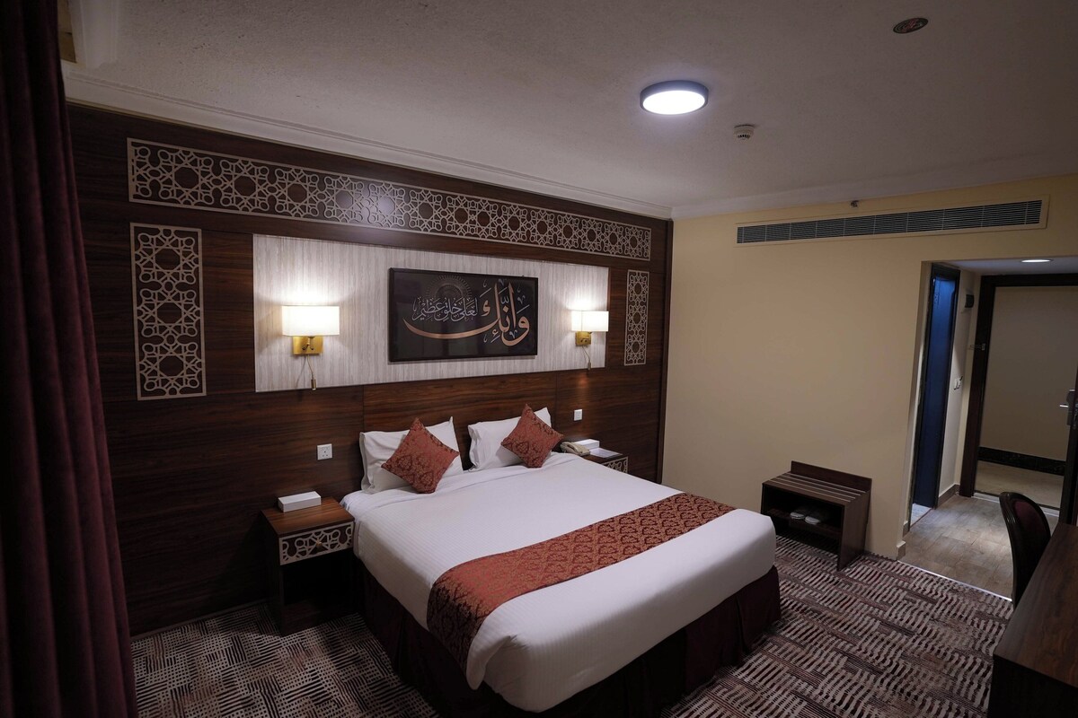 Una habitación de hotel con una cama grande, dos lámparas de noche, un cabecero decorativo y una obra de arte colgada en la pared.