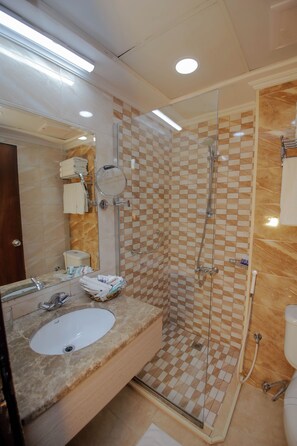 Une salle de bain moderne avec une douche à parois de verre, un lavabo doté d’un plan de travail en marbre et un grand miroir.