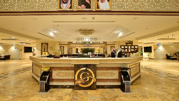 A hotel reception area with a marble floor, a reception desk, and three framed portraits above it. - Abraj Al Tayseer Tuwa Hotel (Makkah)