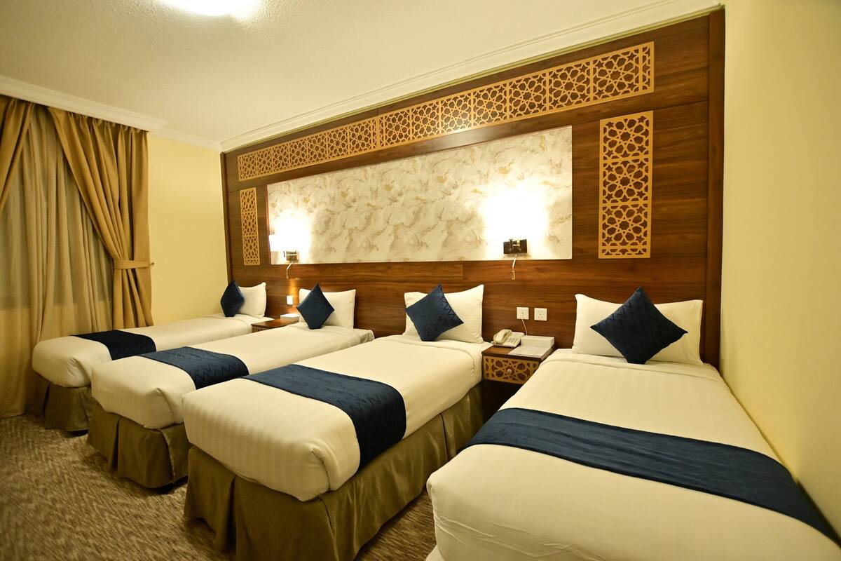 A hotel room with four single beds, a wooden headboard, a marble-patterned wall, and a carpeted floor.