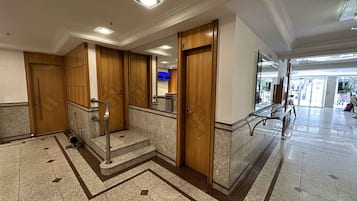 Eine Hotelhalle mit Marmorboden, Holztüren und einem Glaselevator.