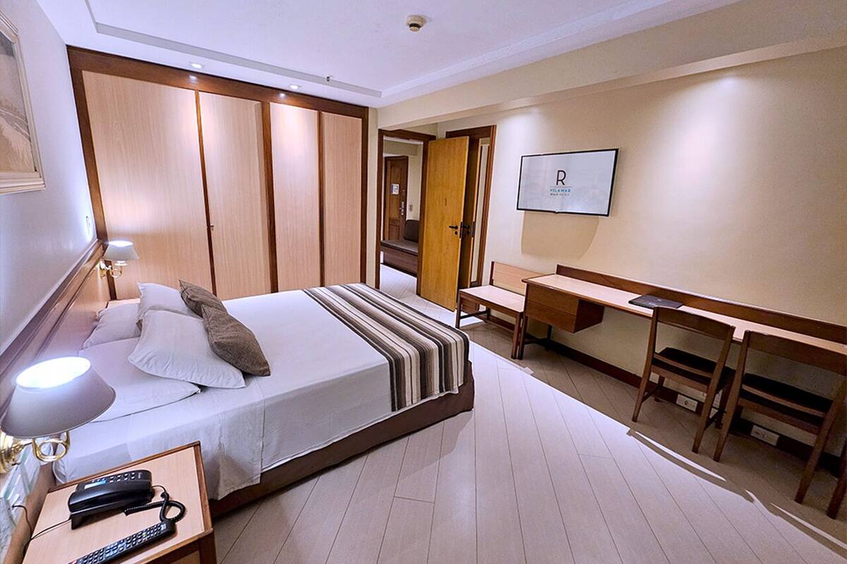 Habitació d'hotel amb llit, taula de nit amb làmpada, escriptori i cadira.