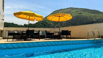 Una piscina al aire libre, sombrillas, sillones reclinables de piscina