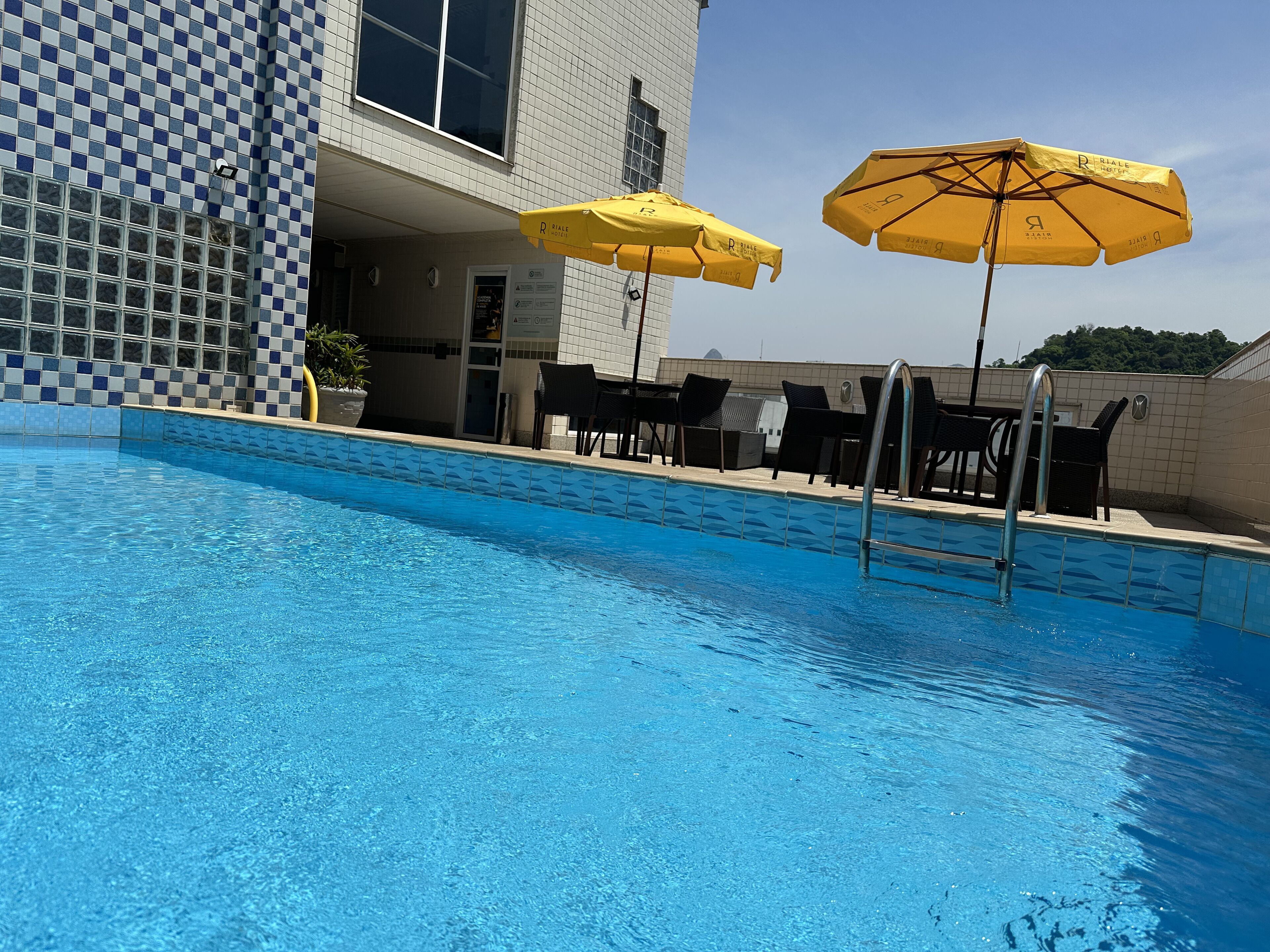 Una piscina con un diseño de baldosas a cuadros, sombrillas amarillas y sillas de descanso negras.