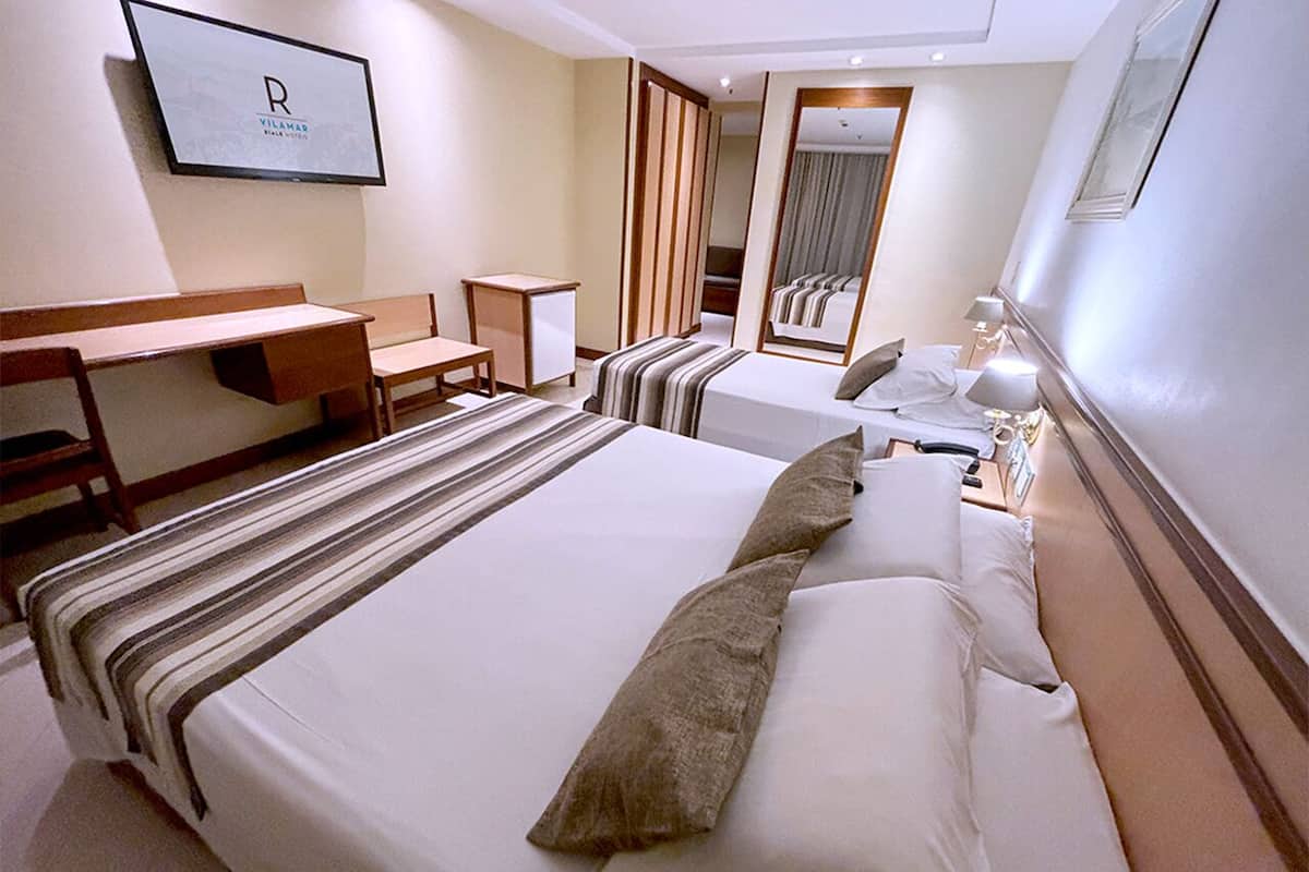 Una habitació d'hotel amb un llit gran, una taula de treball i un mirall.