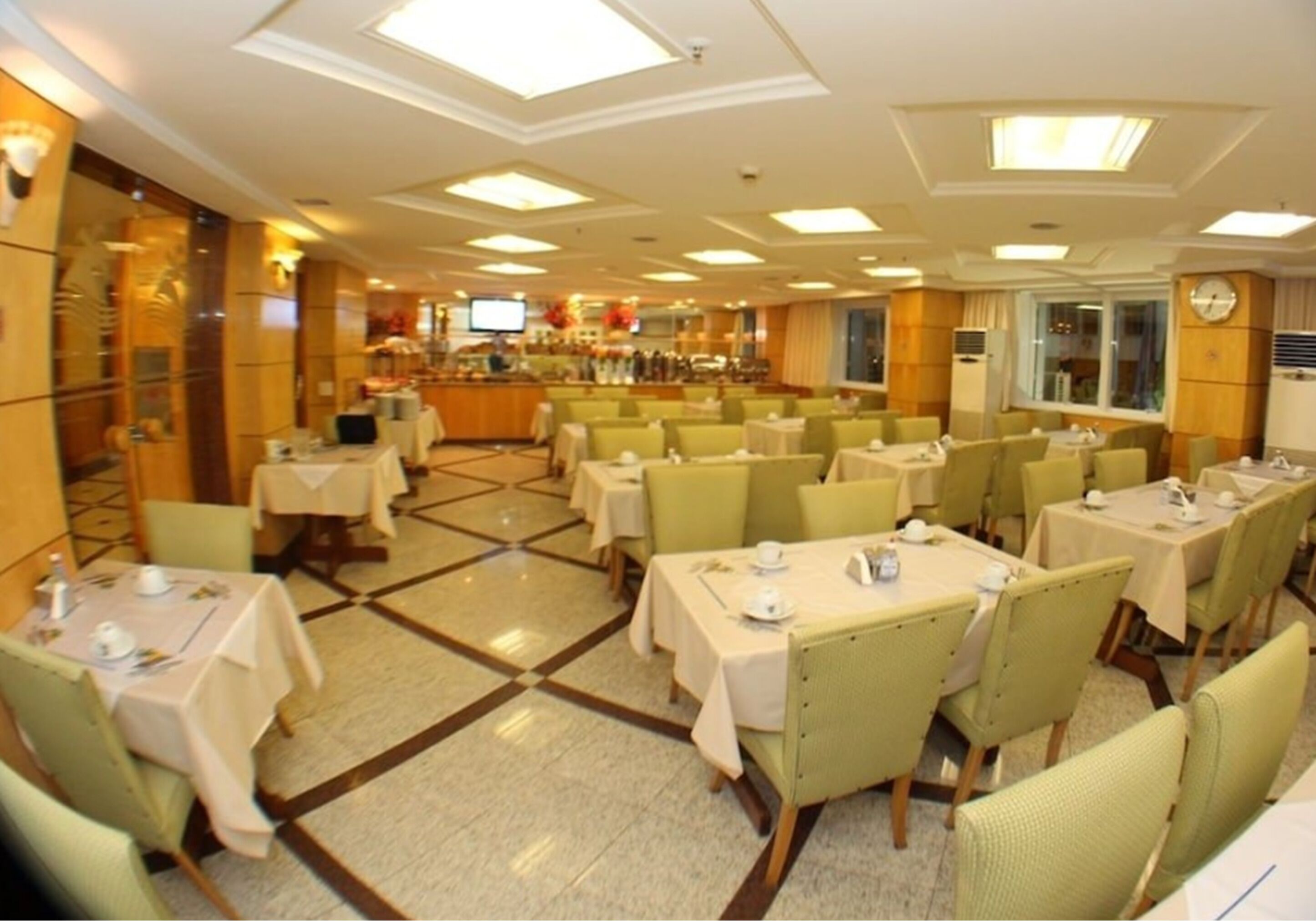A hotel dining area with multiple tables and chairs, a buffet in the background, and a clock on the wall.