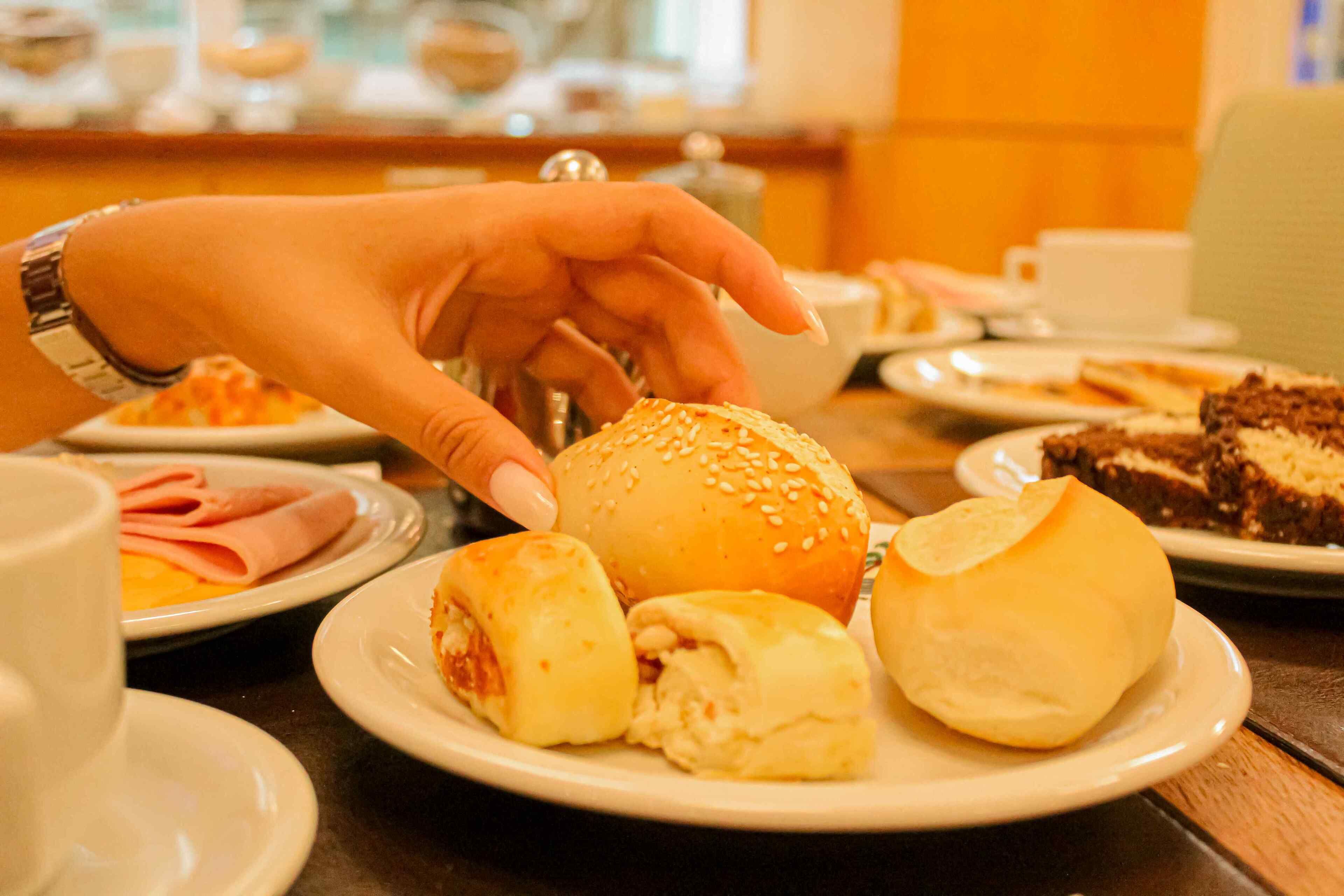 Une table sur laquelle on trouve divers aliments, notamment un pain aux graines de sésame, une part de gâteau et une assiette avec un sandwich au jambon.