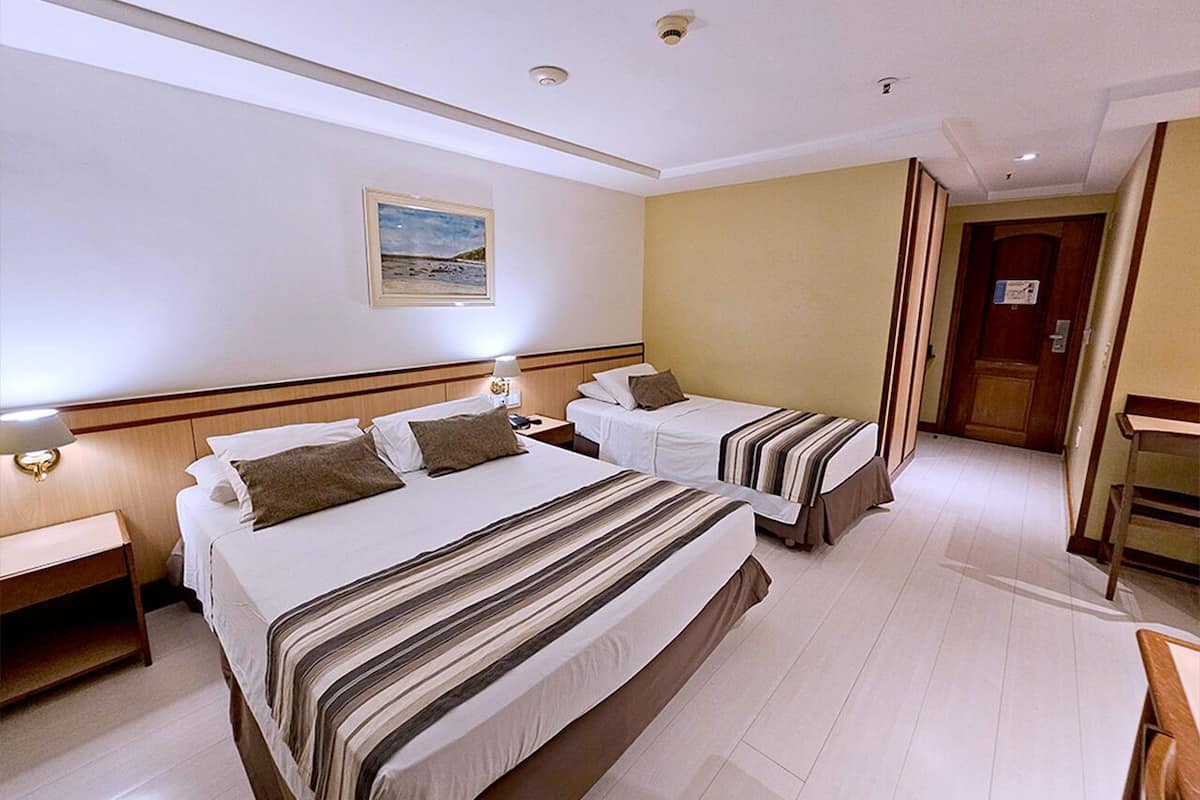 Habitació d'hotel amb dos llits, una taula de nit, un escriptori i una porta que dona a una altra habitació.