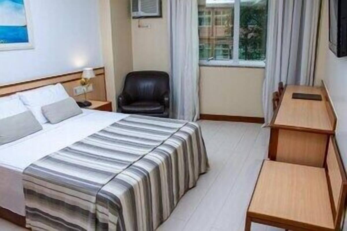 Habitació d'hotel amb un llit, un escriptori, una cadira, una finestra amb cortines i un televisor fixat a la paret.