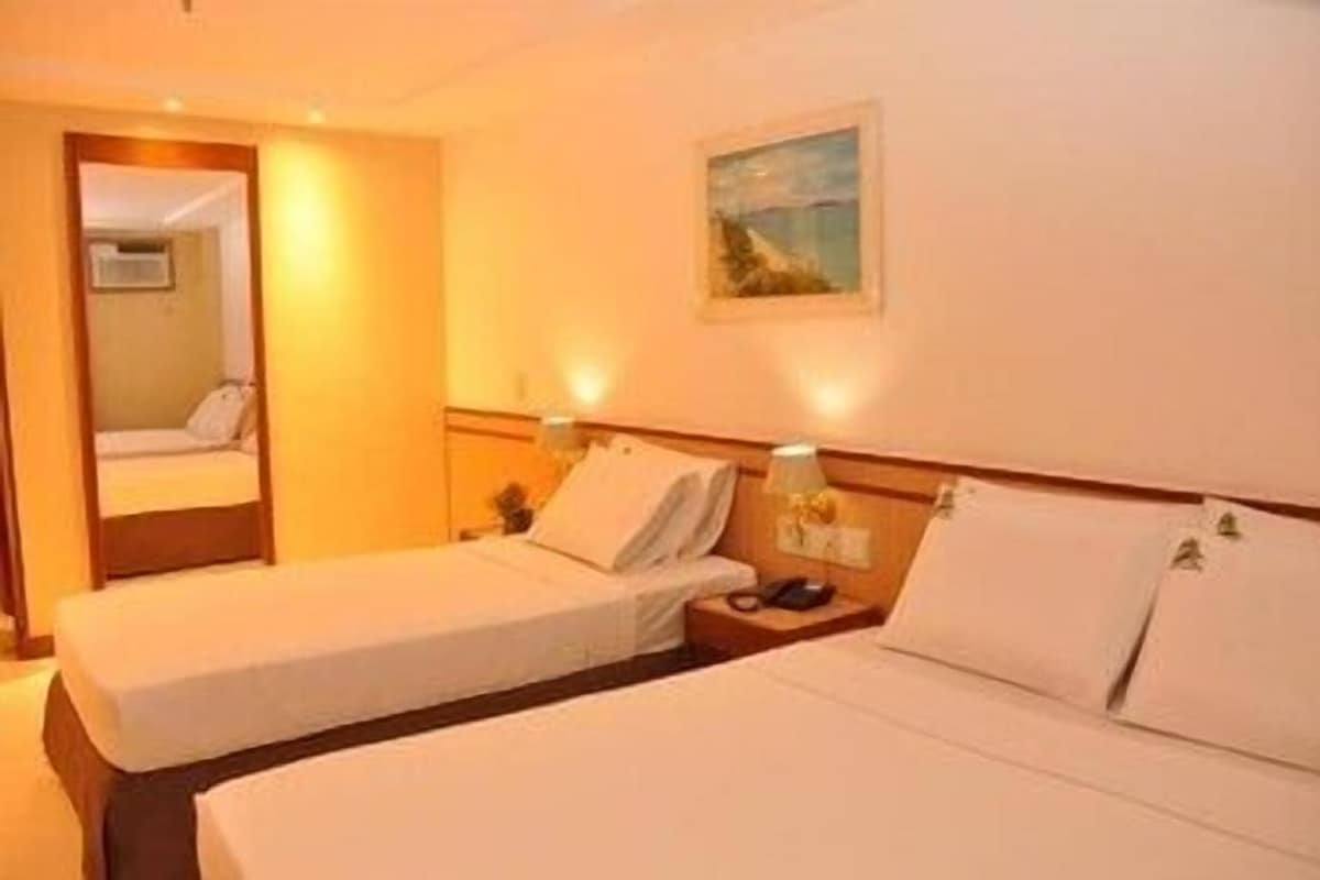Una habitación de hotel con dos camas individuales, mesitas de noche con lámparas, un cuadro en la pared y un espejo.