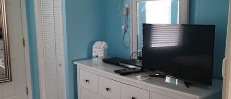 A room with a white dresser, a television, and a window with blinds.