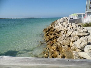 A rocky shoreline with clear water, a wooden deck, and a white fence with a chair. - Island's End Resort (St. Pete Beach)