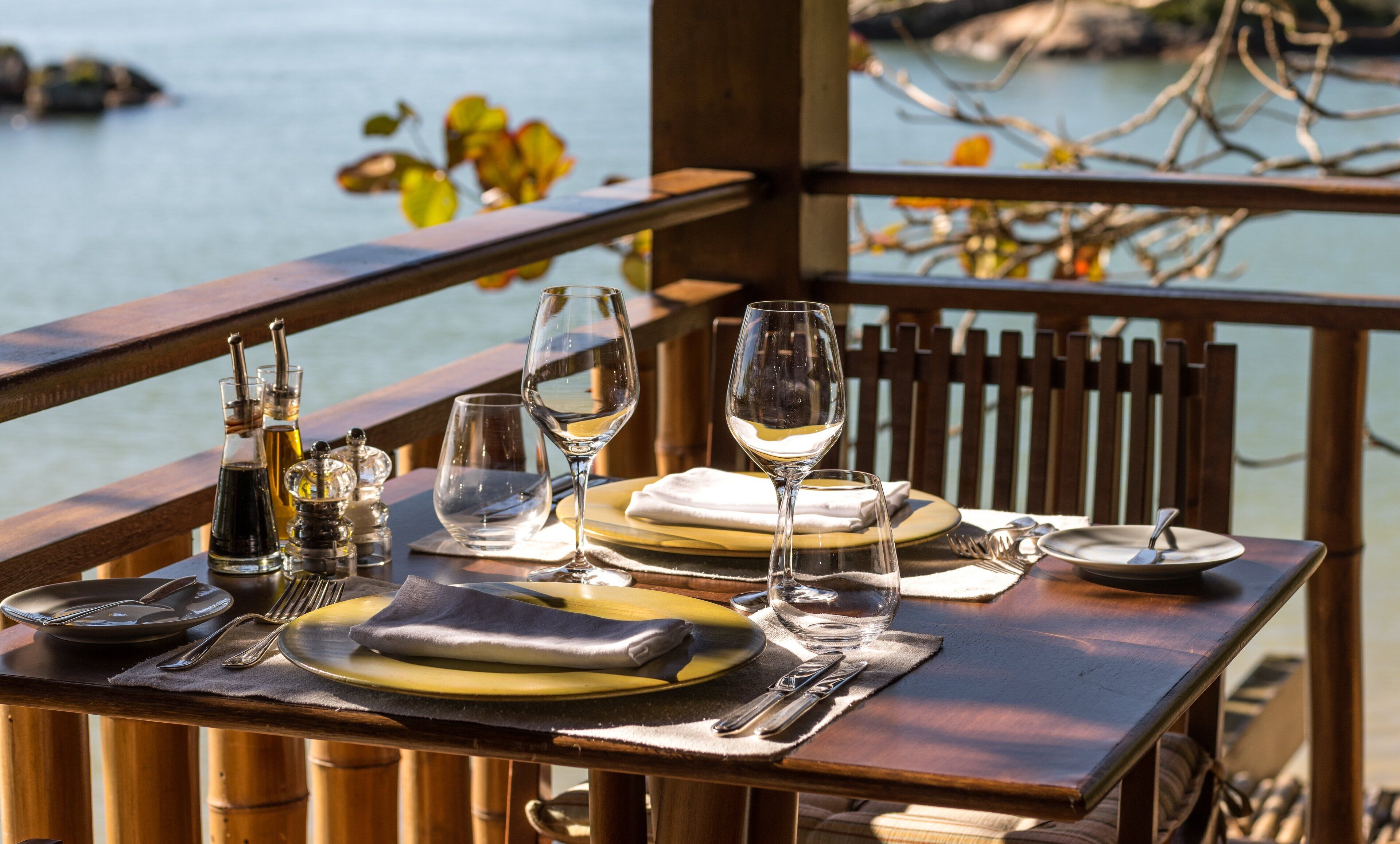 A table set for dining with wine glasses, plates, and cutlery, overlooking a body of water.