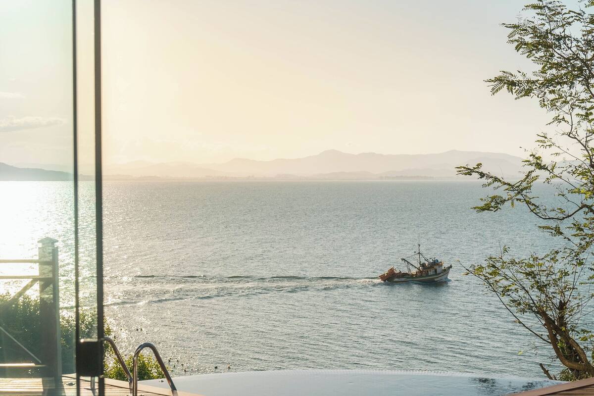 A wooden deck with a glass railing overlooking a calm sea and a boat.