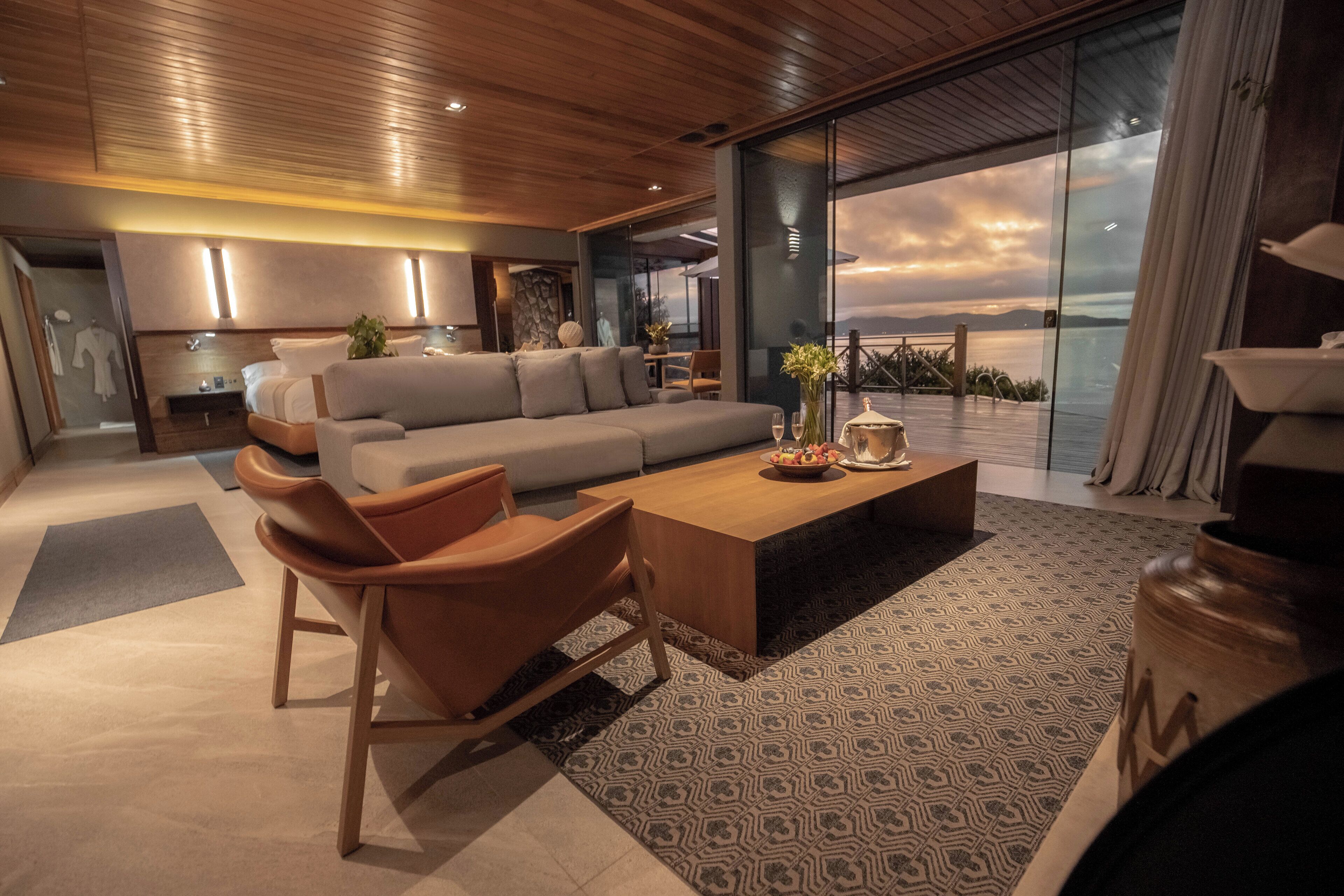 A modern living room with a large sofa, a coffee table, and a view of the ocean.
