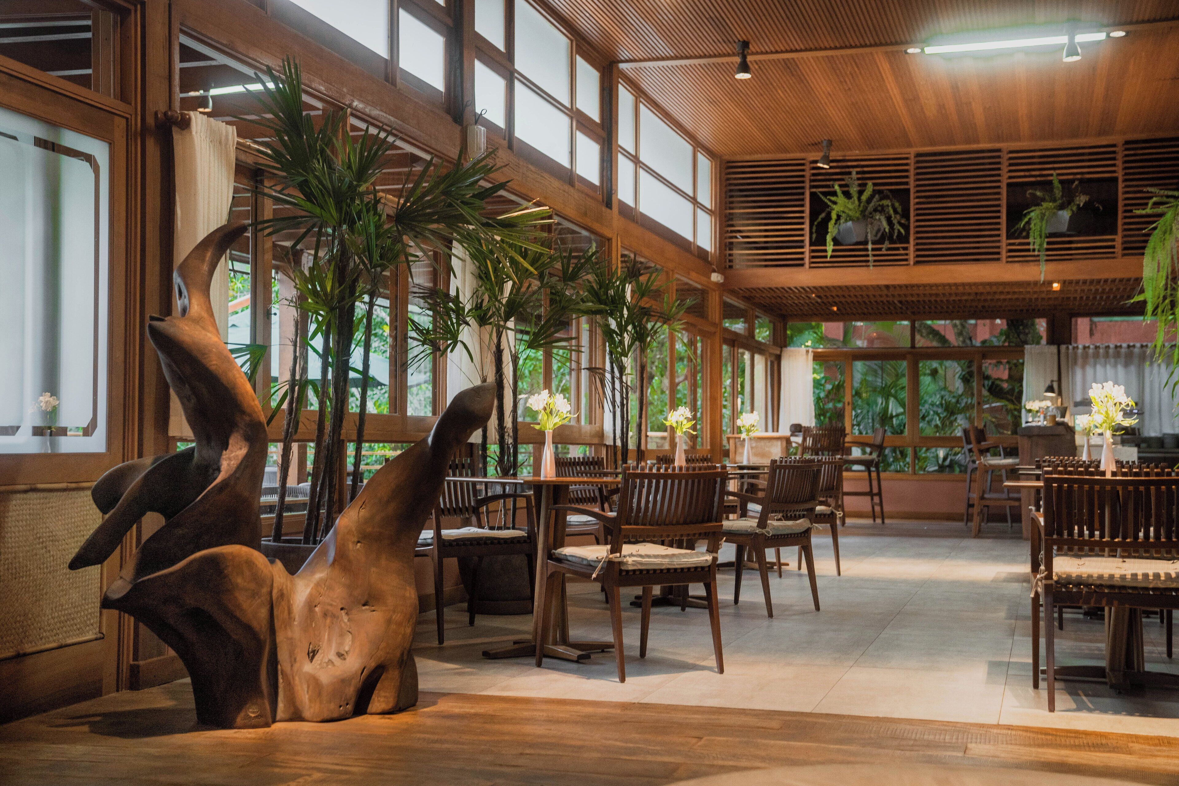 A spacious indoor area with wooden furniture, large windows, and potted plants.