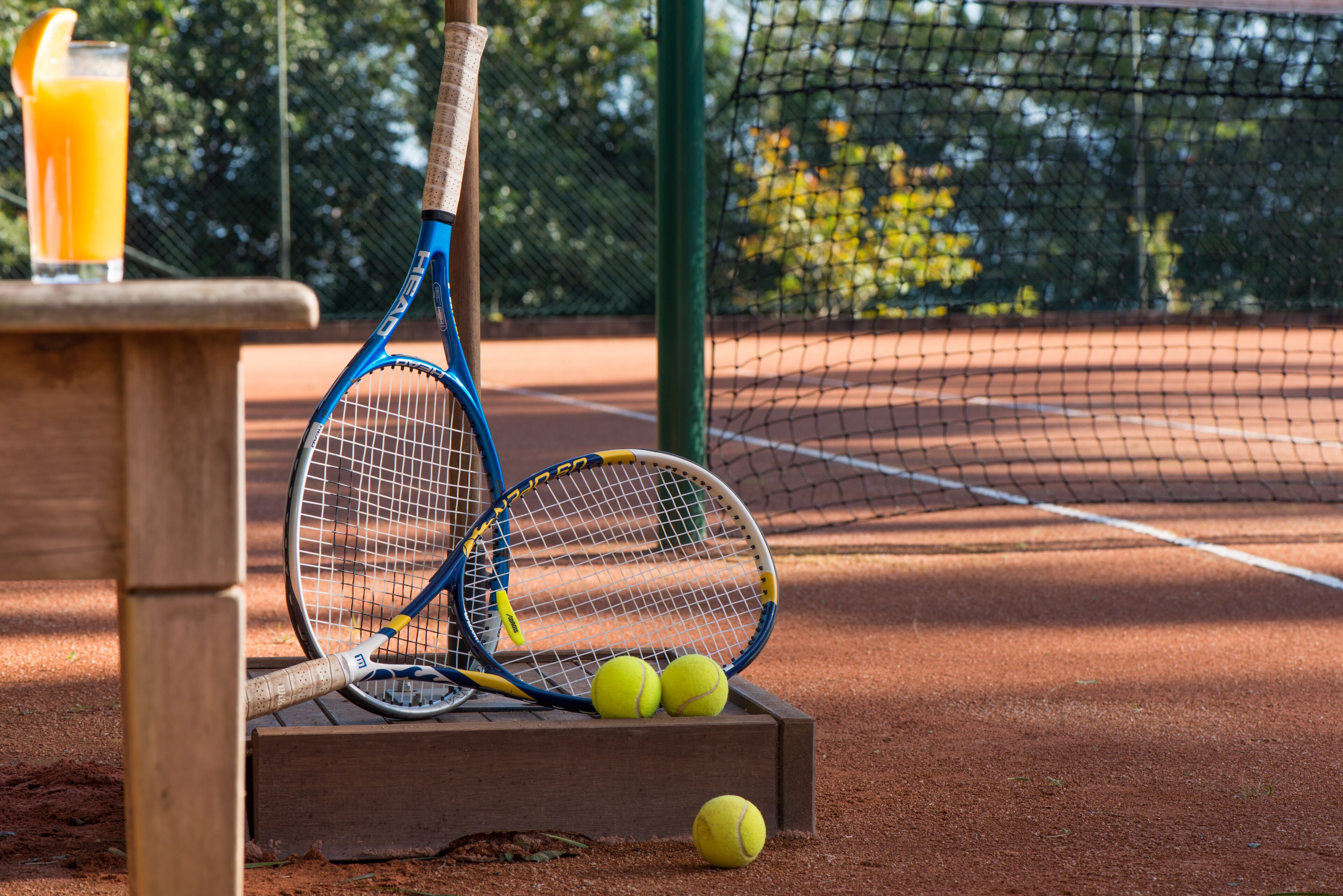 Una cancha de tenis con dos raquetas y tres pelotas sobre un banco de madera.