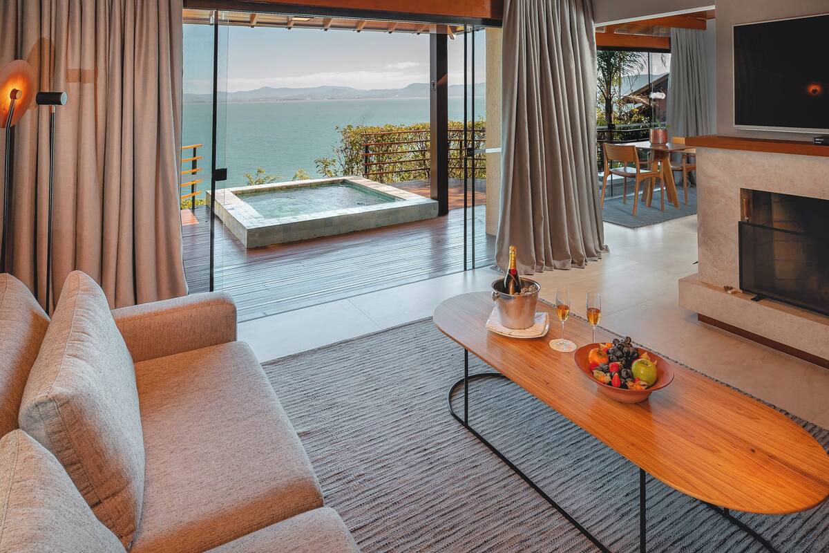A modern living room with a sofa, a wooden coffee table with fruit, a fireplace, and a large TV.
