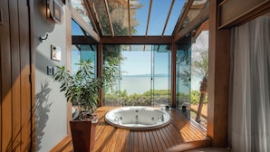 A modern bathroom with a wooden floor, a freestanding bathtub, and a large window offering a view of the sea. - Awasi Santa Catarina (Governador Celso Ramos)
