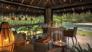 An outdoor dining area with a thatched roof, wicker furniture, and a view of a beach and water. - Awasi Santa Catarina (Governador Celso Ramos)