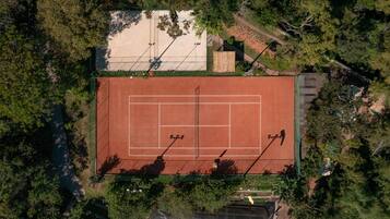 An aerial view of a tennis court surrounded by dense trees.