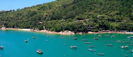 Una zona costera con numerosos barcos en aguas turquesas, una playa arenosa y un promontorio cubierto de bosque denso.