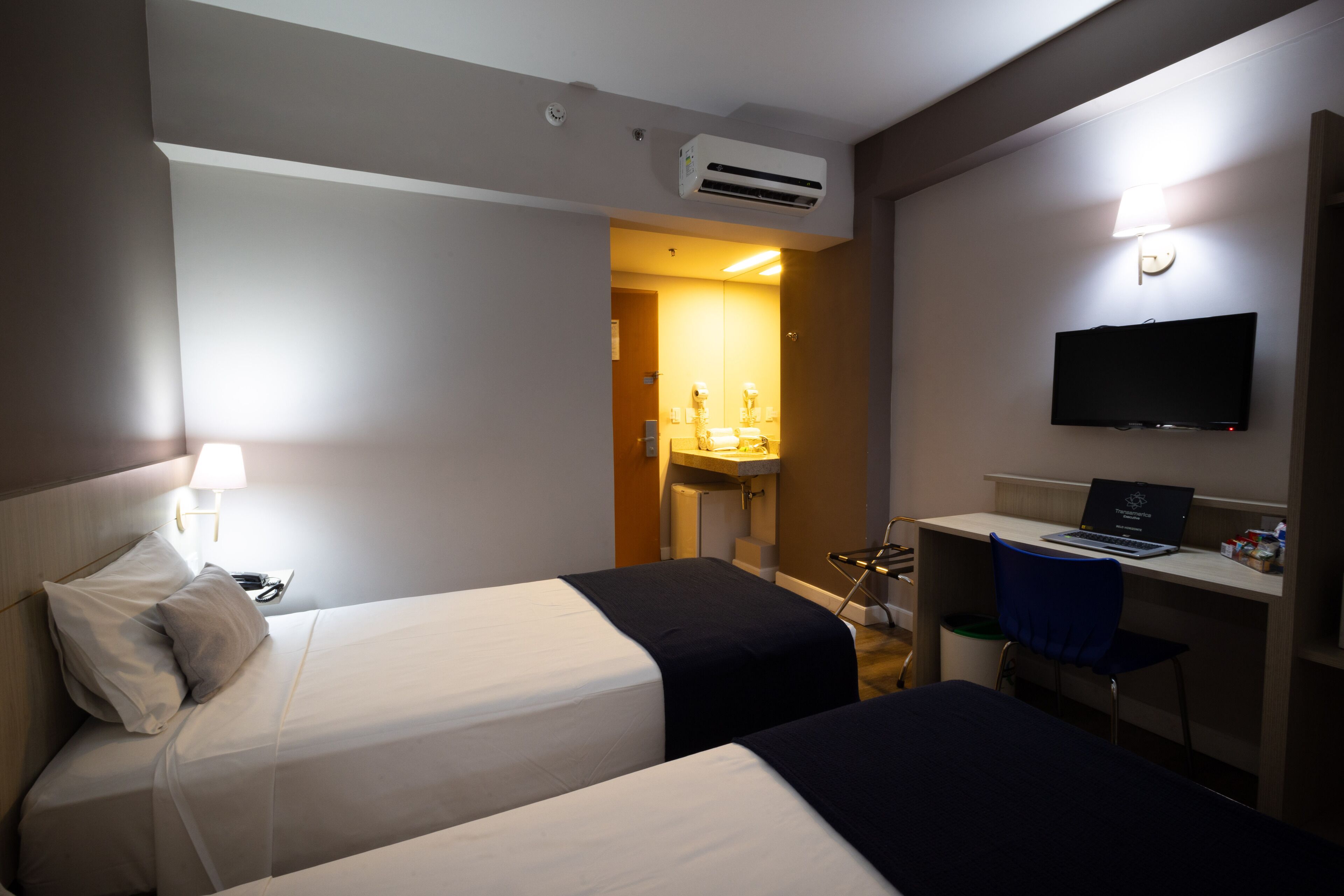 Une chambre d’hôtel avec deux lits, un bureau, un téléviseur à écran plat et un appareil de climatisation.