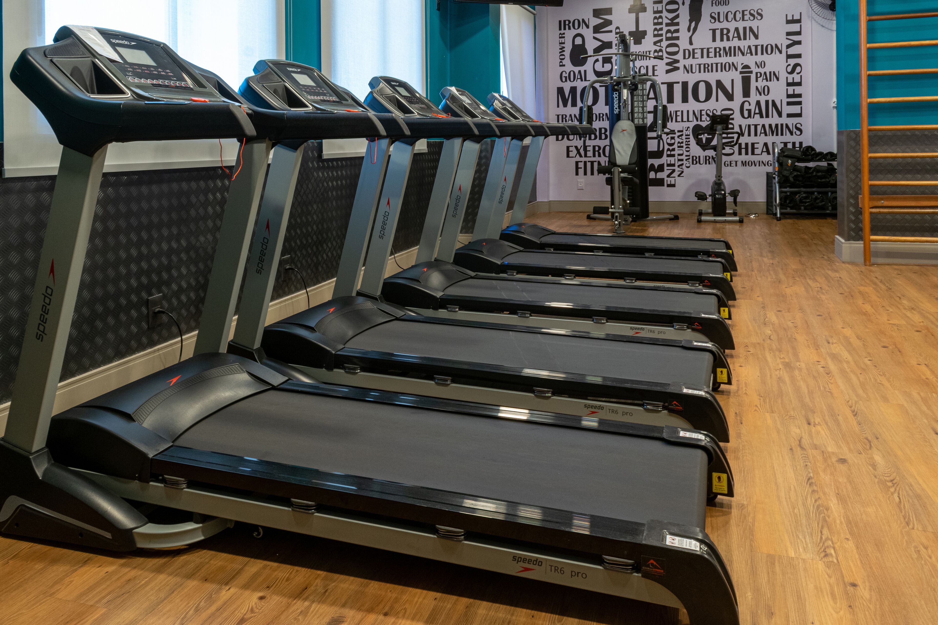 Varias caminadoras en un gimnasio, con un letrero motivacional al fondo.
