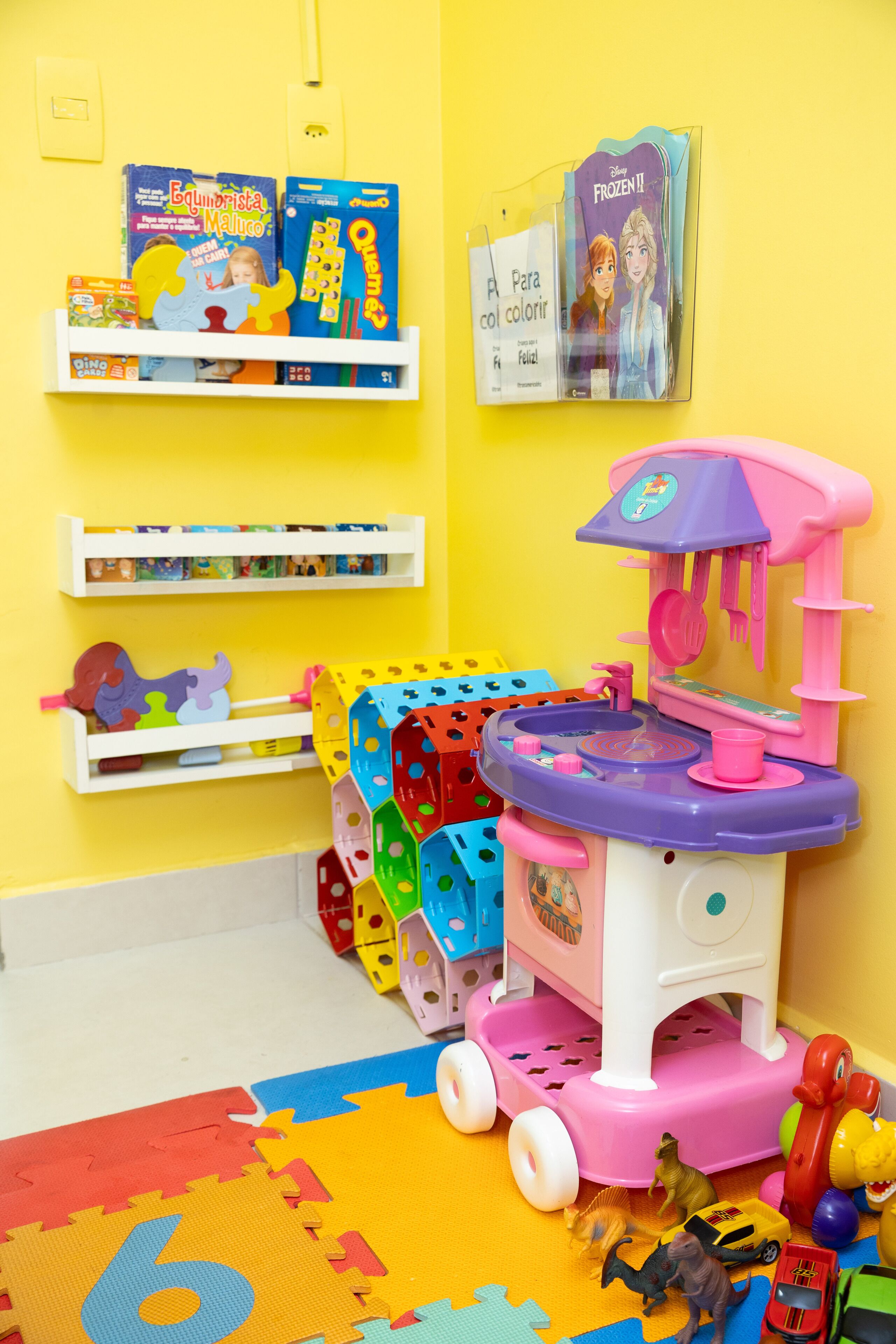 A child's playroom with a toy kitchen set, educational books, and a puzzle mat.