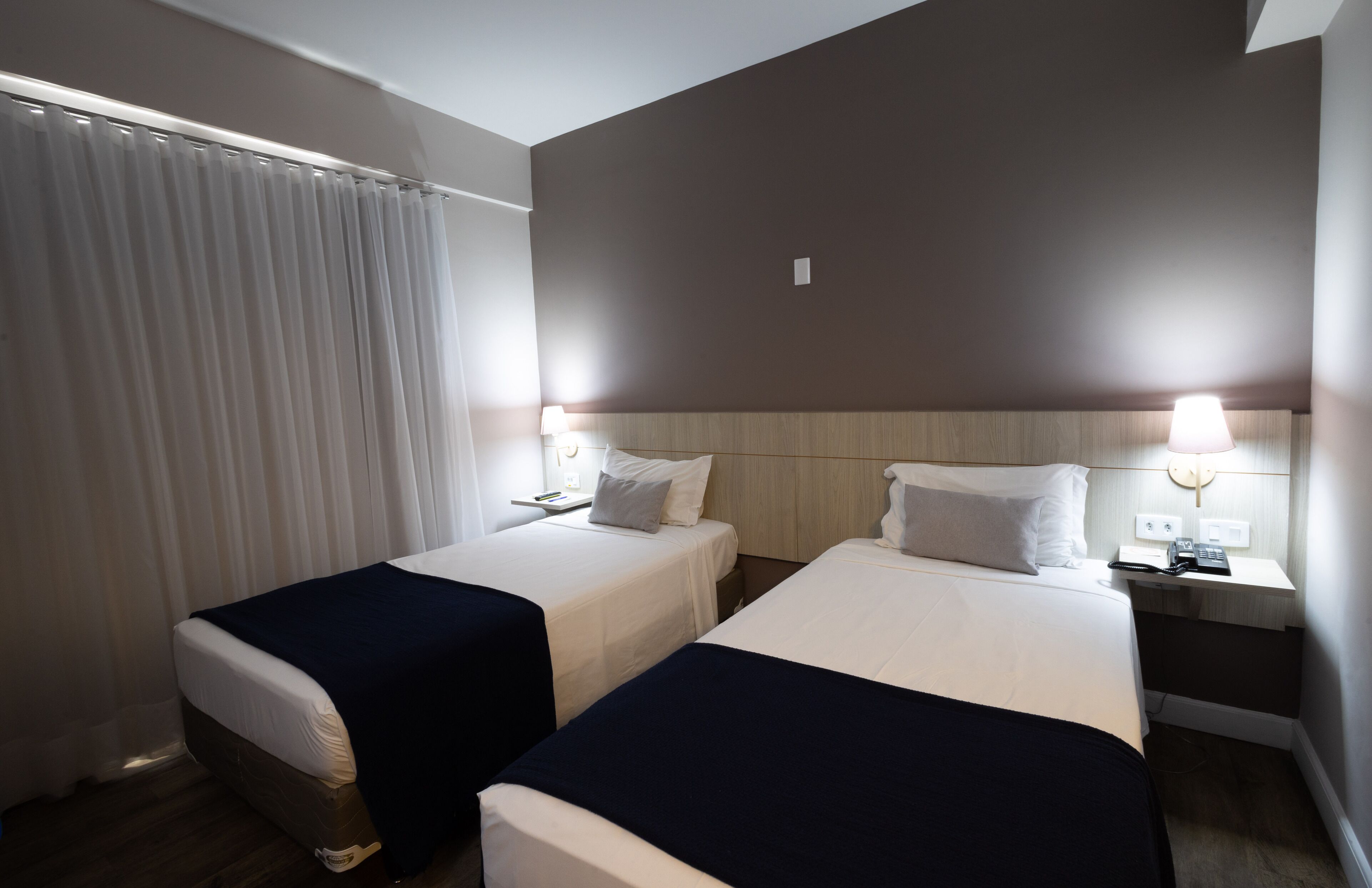 Habitació d'hotel amb dos llits, una nit falda amb una làmpada i una finestra amb cortines.