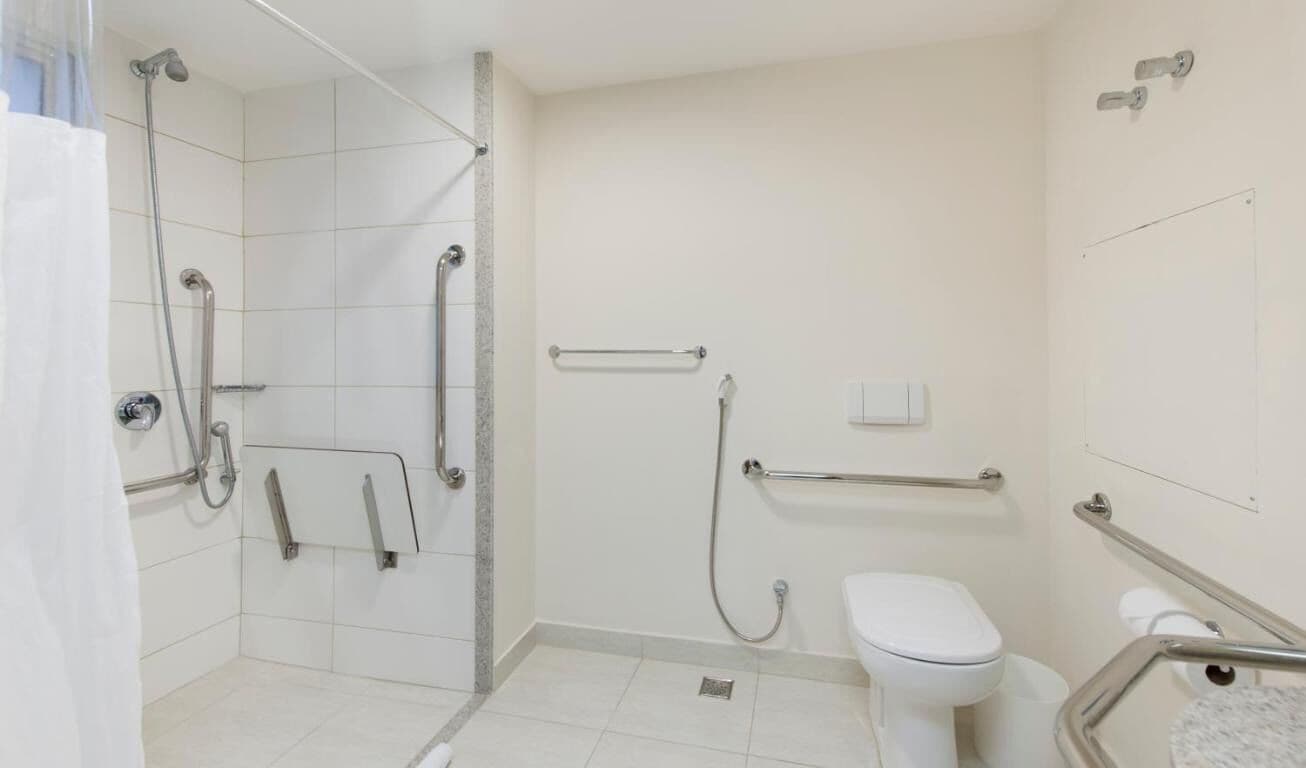 Un baño con ducha, inodoro y barras de apoyo.