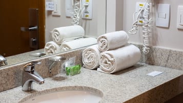 A hotel bathroom with a granite countertop, a sink, two hair dryers mounted on the wall, and several neatly rolled towels.