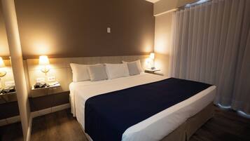 Quarto de hotel com uma cama grande, abajures, telefone e janela com cortinas.