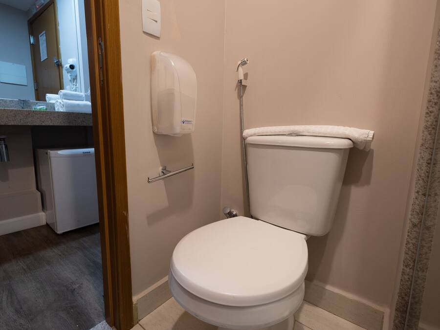 Un baño con inodoro, secador de manos y un refrigerador pequeño.