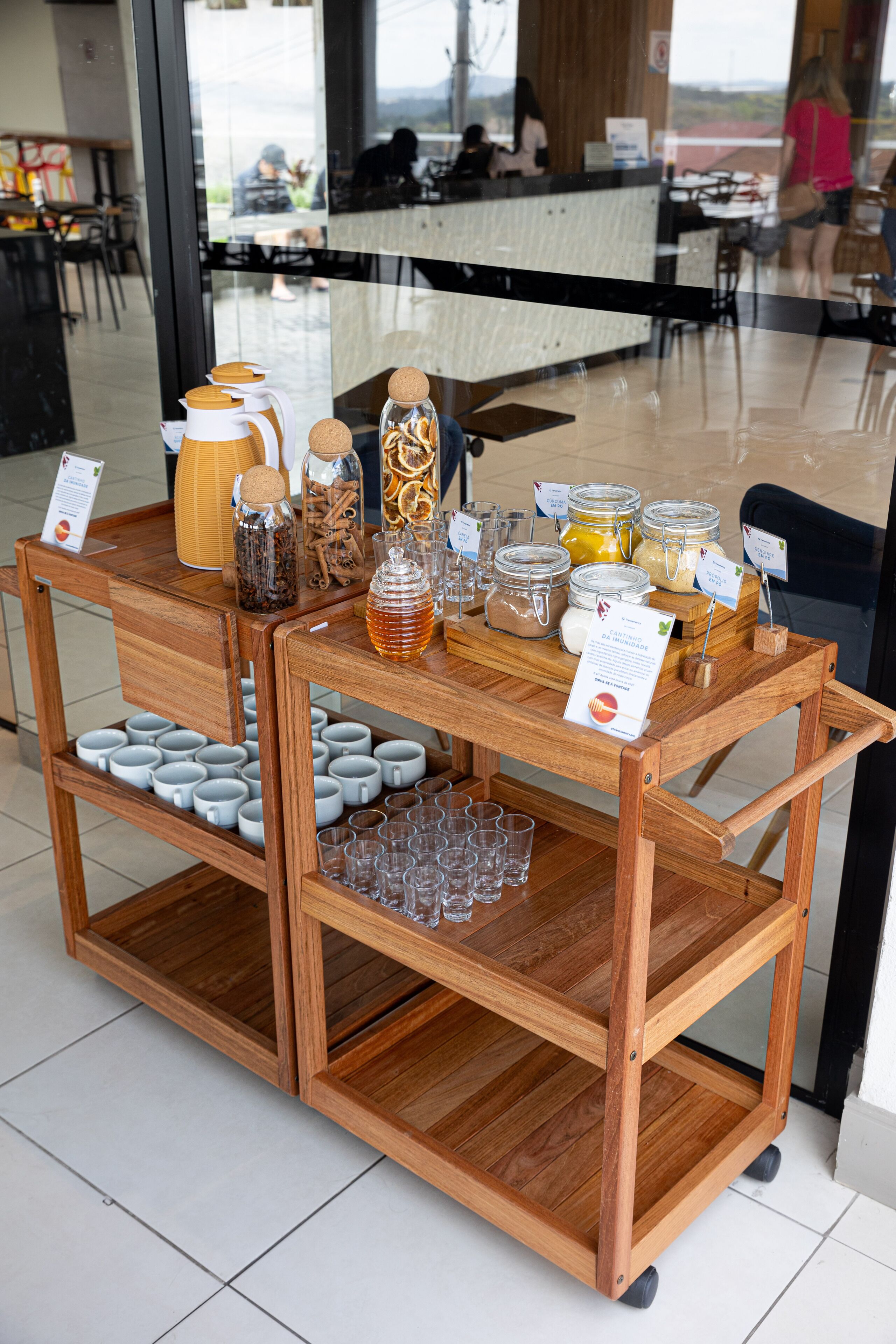 Un carro de madera con frascos de condimentos, un dispensador de miel y un cartel que muestra la carta de bebidas.