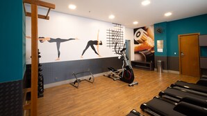 Un gimnasio con equipo de ejercicio, una pared con ilustraciones de fitness y un suelo de madera.