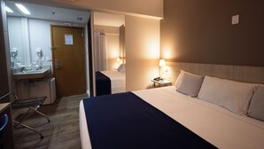 Habitación de hotel con cama, mesita de noche, lámpara y escritorio con silla.