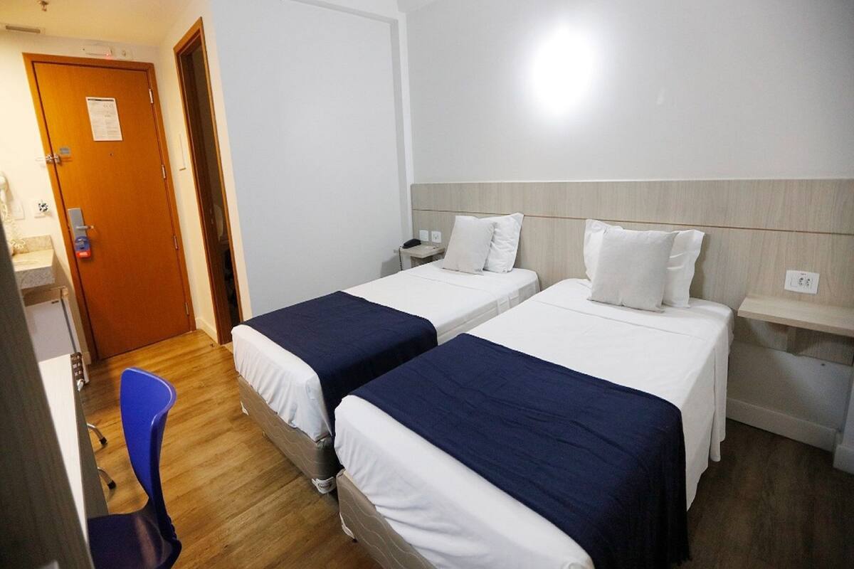 A hotel room with two single beds, a desk, a chair, and a wooden floor.